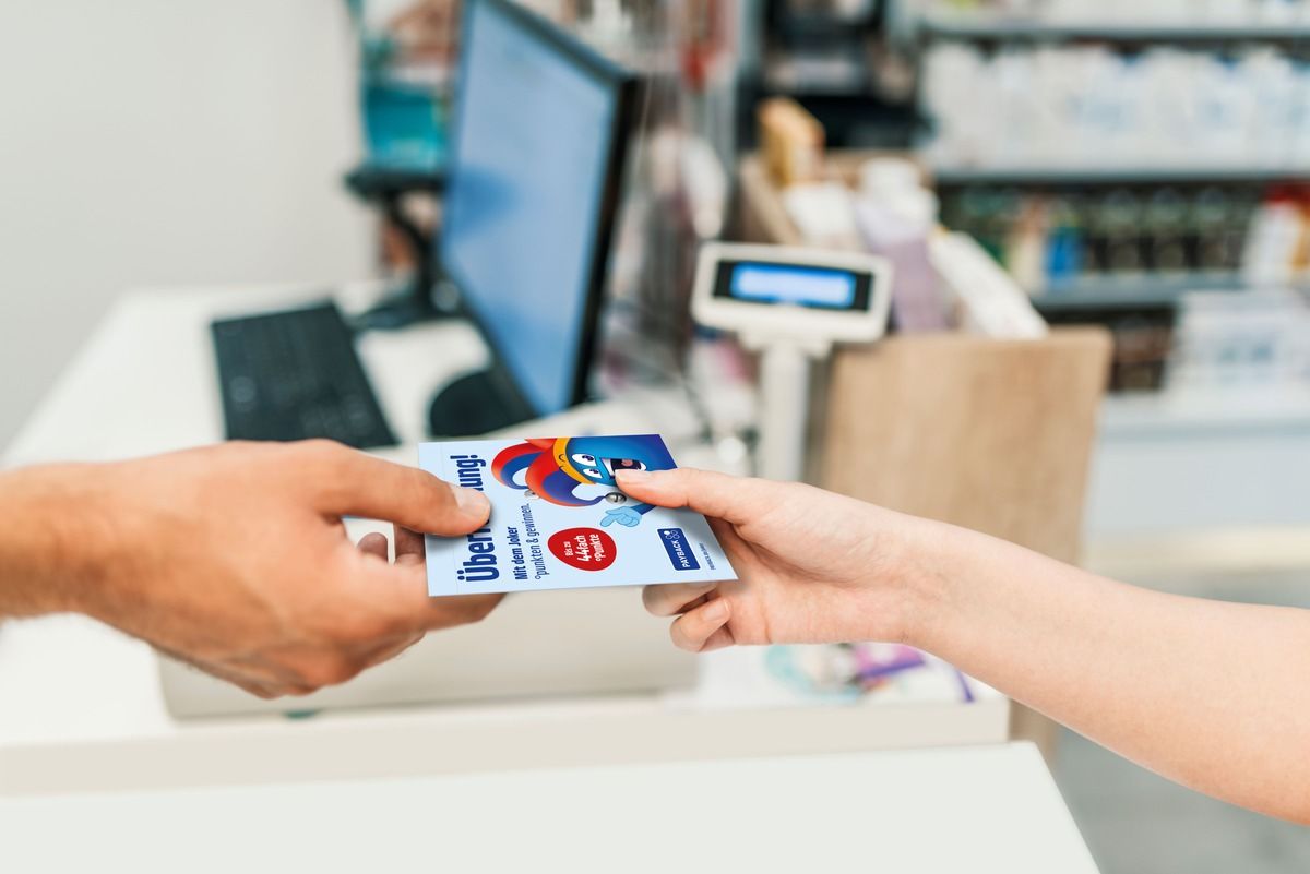 Eine Hand reicht an einer Ladenkasse ein Couponheft der Payback-Joker-Aktion weiter